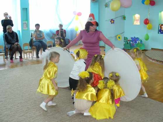 Педагог держит два больших круга перед девочками в жёлтых костюмах
