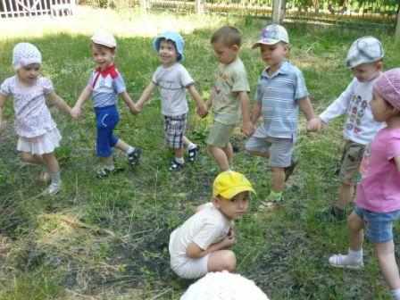 Дети стоят полукругом на траве, в центре сидит мальчик