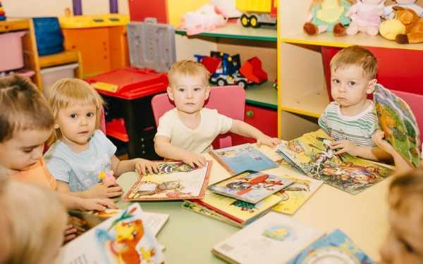 Малыши в детском саду сидят за столом с книжками
