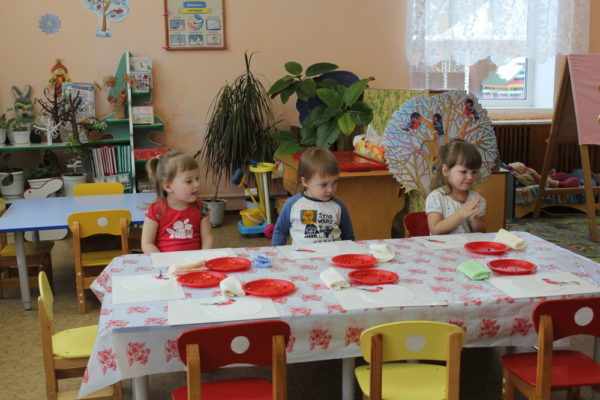 Трое детей сидят за столиками с красными тарелками
