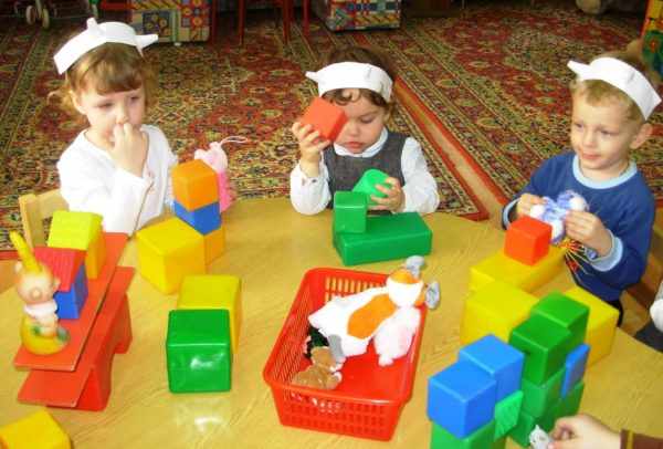 Трое детей в шапочках с рожками строят домики из кубиков