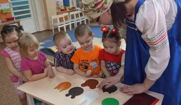 Воспитательница в русском сарафане помогает детям обрисовывать шаблоны мордочек животных
