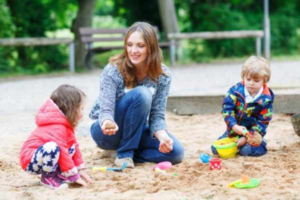 Два ребёнка и воспитатель играют в песочнице