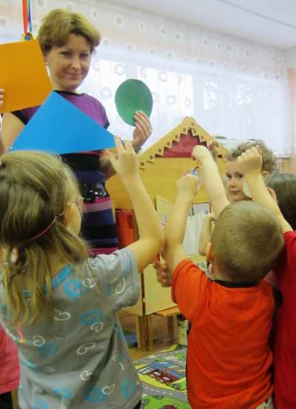 Воспитатель и дети держат в руках геометрические фигуры