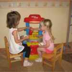 Две девочки играют с большой детской кухней