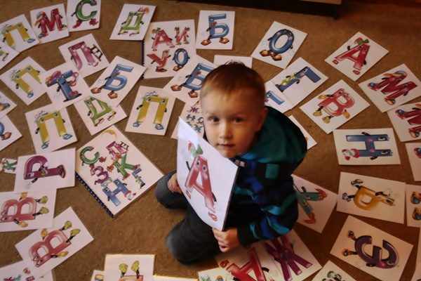 Мальчик, окружённый изображениями букв, в руках держит картинку с буквой А