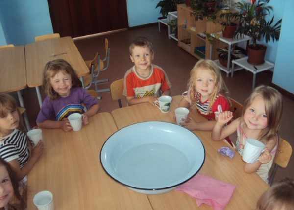 Дети сидят за столом, по центру которого миска с водой