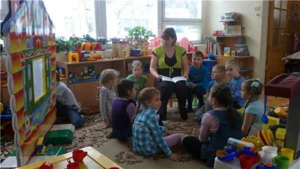 Воспитатель с книгой на коленях беседует со старшими дошкольниками