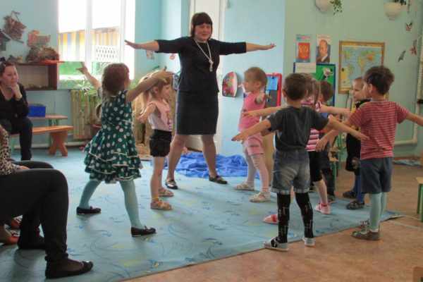 Дети и педагог стоят на ковре, вытянув руки в стороны