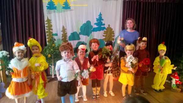 Воспитательница в окружении детей в костюмах и с цветами