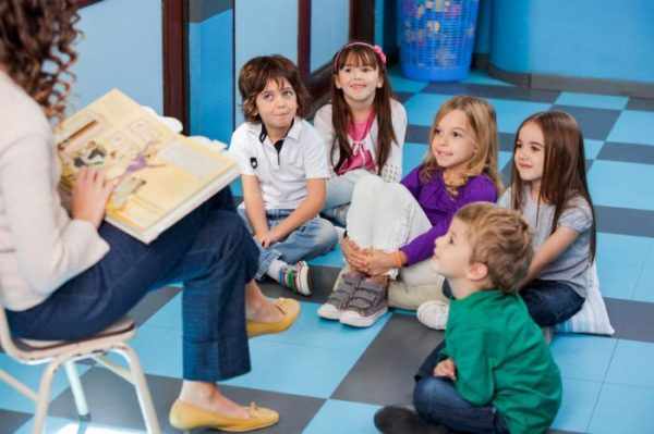 Воспитательница читает книгу сидящим на полу детям