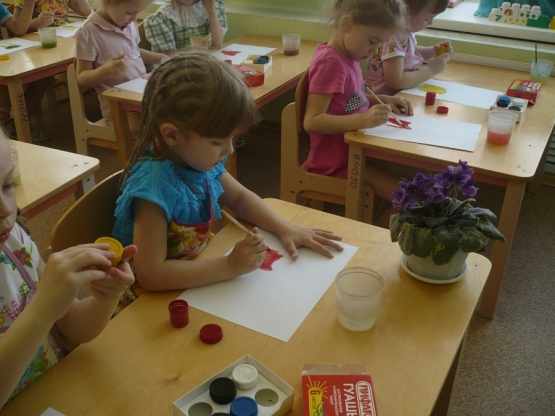 Дети, сидя за партами, рисуют гуашью