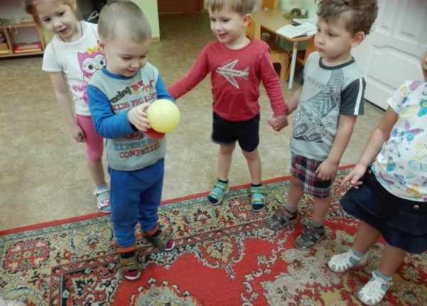 Дети стоят кругом, взявшись за руки, мальчик держит жёлтый мячик