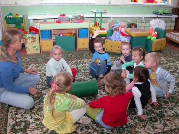 Воспитательница и дети сидят по кругу на коврике