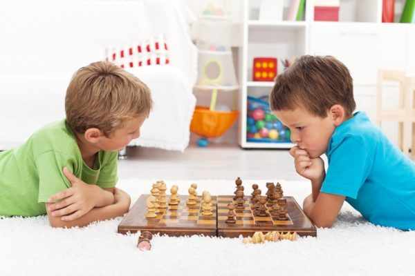 Два мальчика играют в шахматы на полу и размышляют