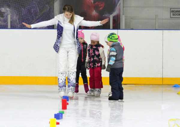 Тренер показывает детям как на коньках объезжать кубики