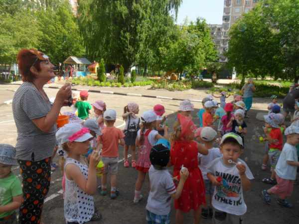 Воспитательница и дети дуют мыльные пузыри на улице