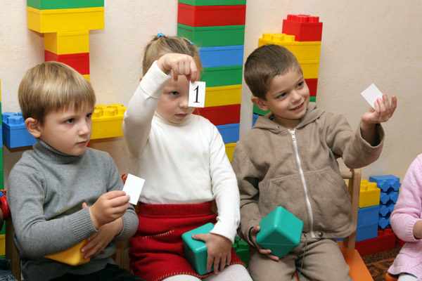 Трое детей держат в руках кубики и карточки с цифрами