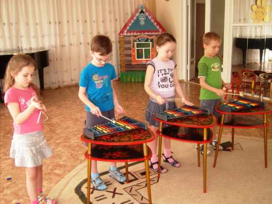 Четыре ребёнка играют на музыкальных инструментах — металлофонах и треугольнике