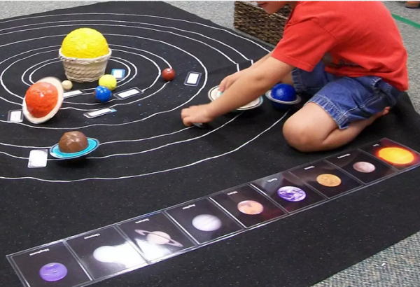 Мальчик выкладывает на ковре модель Солнечной системы