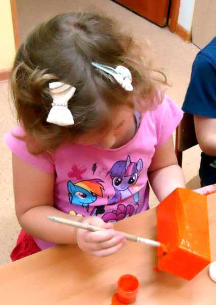 Девочка раскрашивает коробку в оранжевый цвет