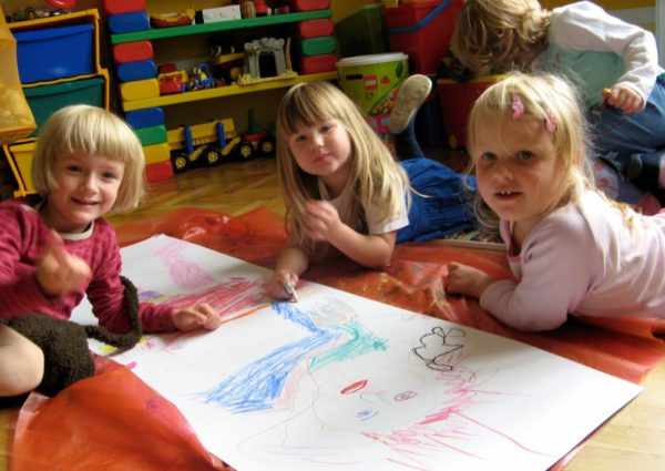 Три девочки, лёжа на полу, рисуют