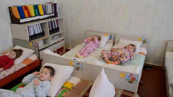 Дети лежат в кроватках в спальне, слева шкаф с папками