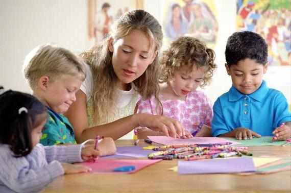 Воспитательница помогает детям рисовать восковыми карандашами