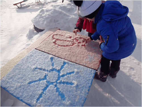 Двое детей рисуют пальцами солнце и цветок на снегу
