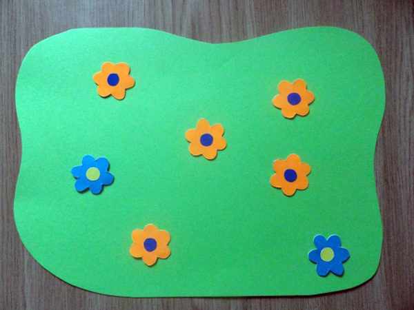 Оранжевые и голубые цветочки разложены на зелёном листе бумаги