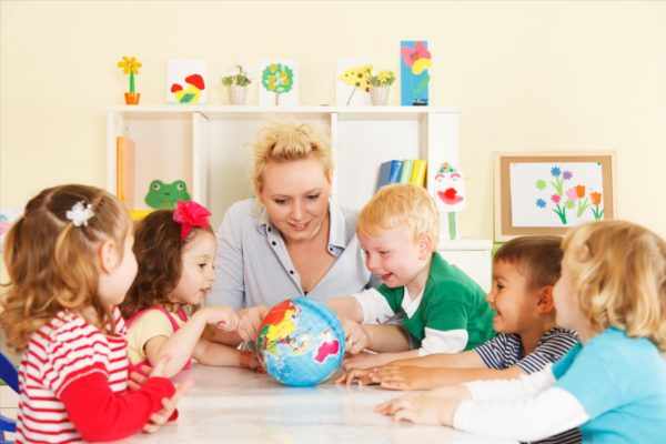 Воспитатель показывает улыбающимся детям глобус