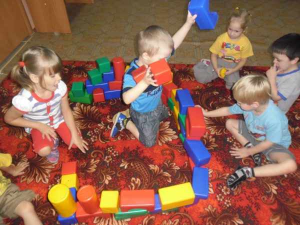 Дети играют на ковре с пластиковыми строительными модулями