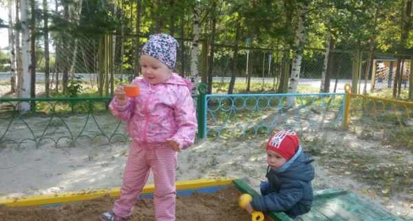Мальчик и девочка, одетые по-весеннему, играют в песочнице