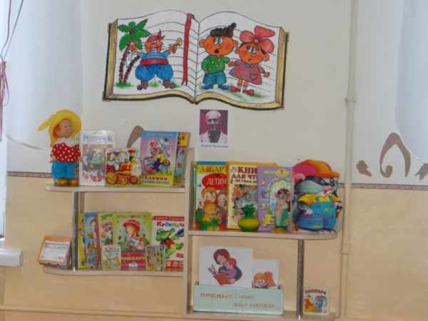 Уголок чтения в детском саду с книгами на полках и иллюстрациями на стене