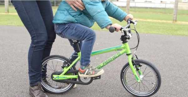 Ребёнок едет на велосипеде, взрослый придерживает его за бока