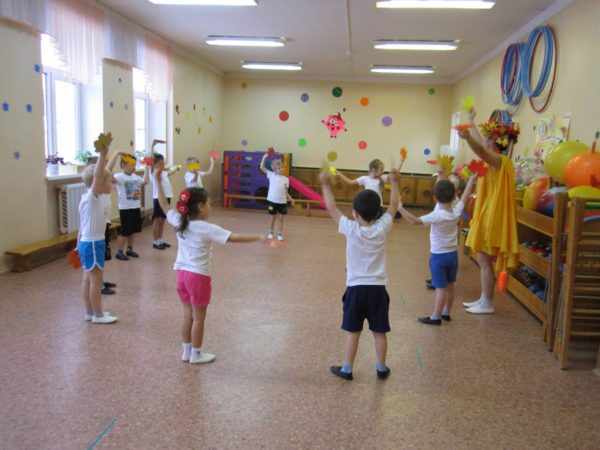 Дети и педагог в костюме Осени стоят в кругу и машут листочками