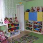 Жёлто-голубой шкаф с нишей, заполненной игрушками, три детские колясочки слева