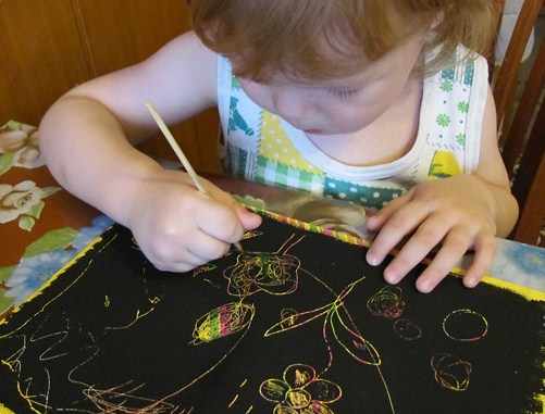 Девочка дошкольного возраста рисует в технике граттаж