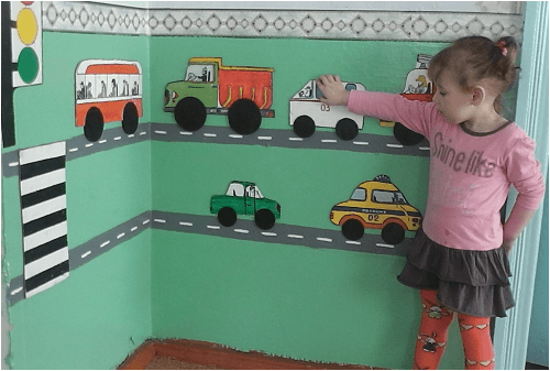 Девочка передвигает машинки на стене с макетом дороги
