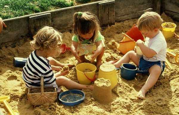 Две девочки и мальчик играют в песочнице