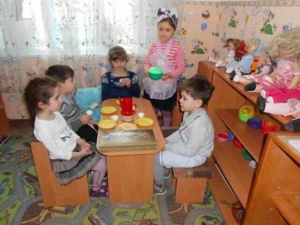 Дети сидят за столом с игрушечной посудкой