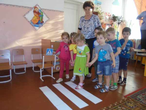 Дети и педагог стоят перед импровизированным пешеходным переходом в помещении группы