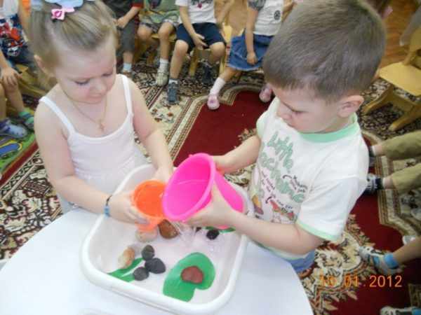Мальчик и девочка наливают в тазик воду из пластмассовых ведёрочек