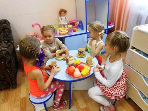 Четыре девочки сидят за столиком с фруктами и чашками