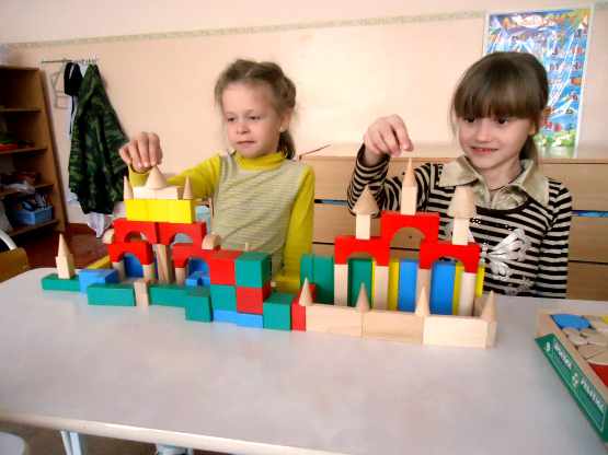 Две девочки строят замки с башнями из деревянных деталей