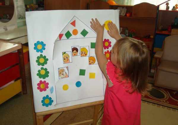 Девочка крепит на лист с изображением домика и людей жёлтый кружочек