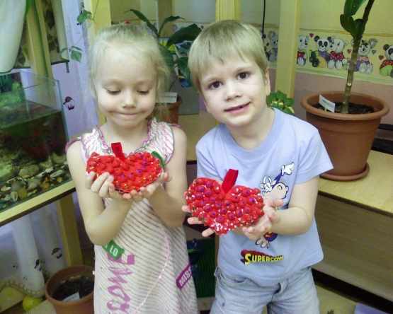 Мальчик и девочка держат в руках поделки — красные сердечки