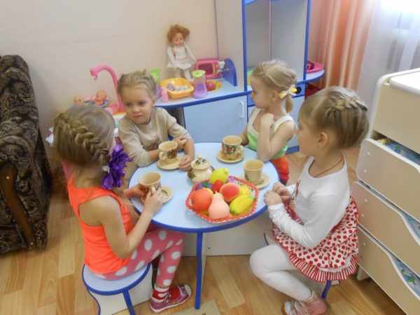 Девочки, сидя за столом с игрушечной посудой, играют в чаепитие