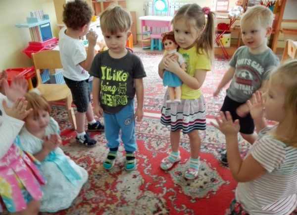 Дети стоят полукругом, девочка прижимает к себе куклу