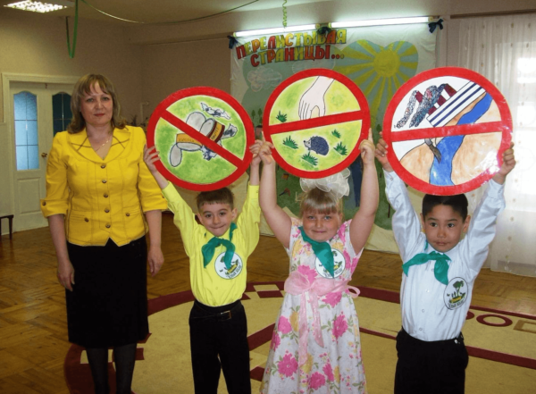 Дети держат запрещающие знаки для отдыхающих на природе, педагог стоит рядом